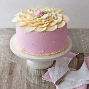 Edgar's Bakery strawberry cake on white cake stand with serving utensil on white and pink napkins in bottom right hand side of frame
