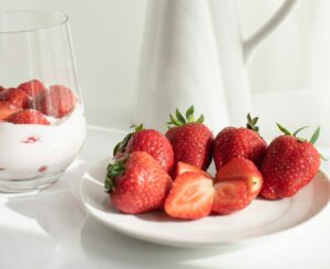 Strawberries on white plate, white vase with flowers, clear glass with yogurt parfait